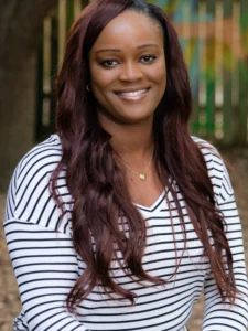 Smiling woman outdoors with long burgundy hair wearing a white and navy striped top.